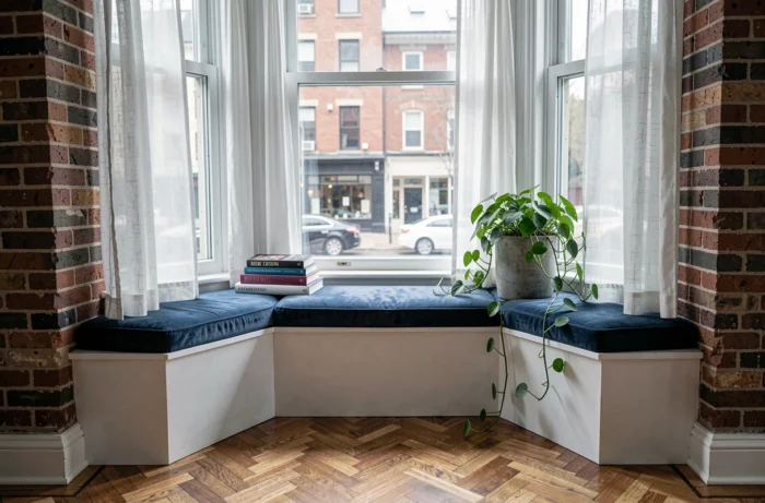 Coin lecture aménagé dans une alcôve avec coussin en velours bleu, livres de design et plante retombante sur parquet en chevrons